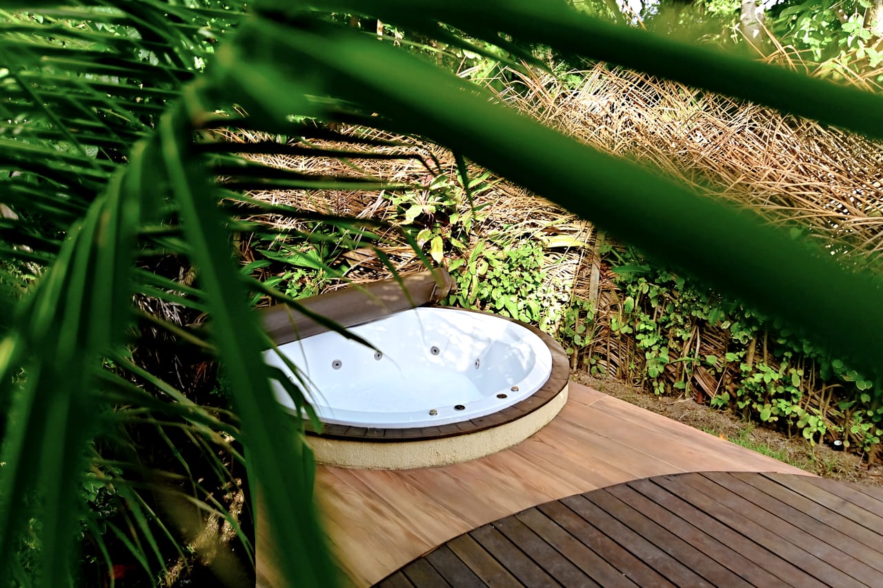 A jacuzzi da Cabana Esmeralda no deck, vista por entre folhas de palmeira