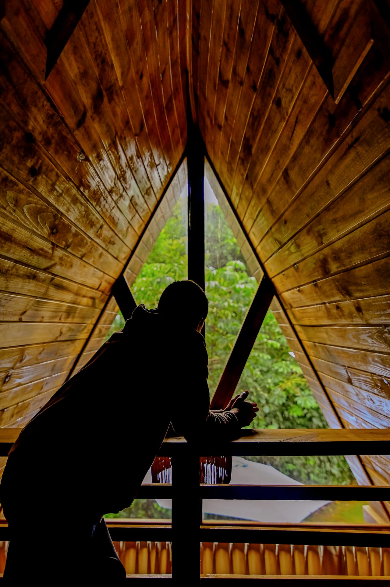 Silhueta de uma pessoa olhando pela janela triangular da cabana