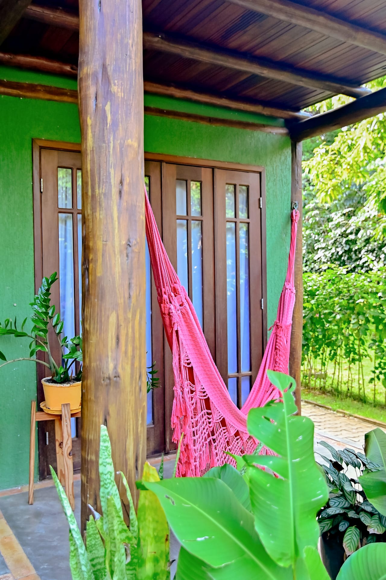 Rede rosa pendurada na varanda do bangalô verde